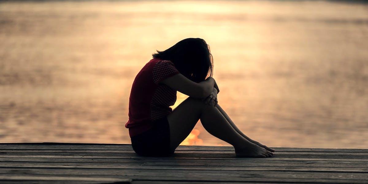 En ledsen kvinna sitter på en brygga. Allt fler drabbas av årstidsbunden depression på sommaren
