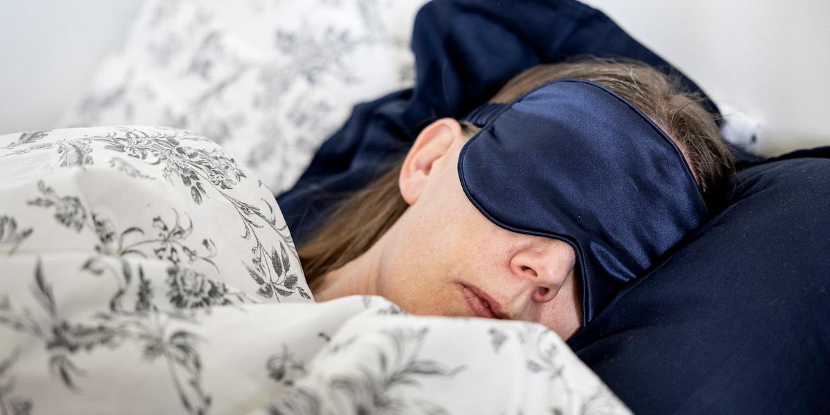 En kvinna sover med en sovmask. Det är bra för din sömn att det är mörkt när du ska sova
