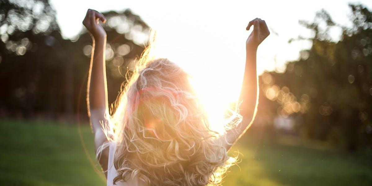 En kvinna tittr mot solen och håller upp armarna i luften. Sommarvärmen ska komma tillbaka till helgen