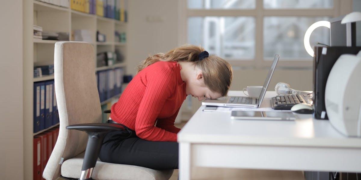 En kvinna har somnat med huvudet på sin dator. Forskning visar att förekomsten av det ofta försvagande tillståndet postcovid, minskade under pandemins gång.