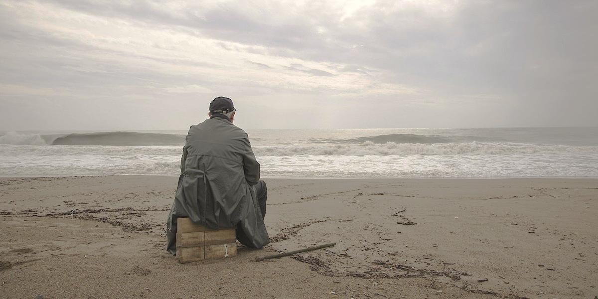 En man sitter på en strand. För att bryta ensamhet behöver man våga kasta sig ut och träffa nya människor och för det krävs mod