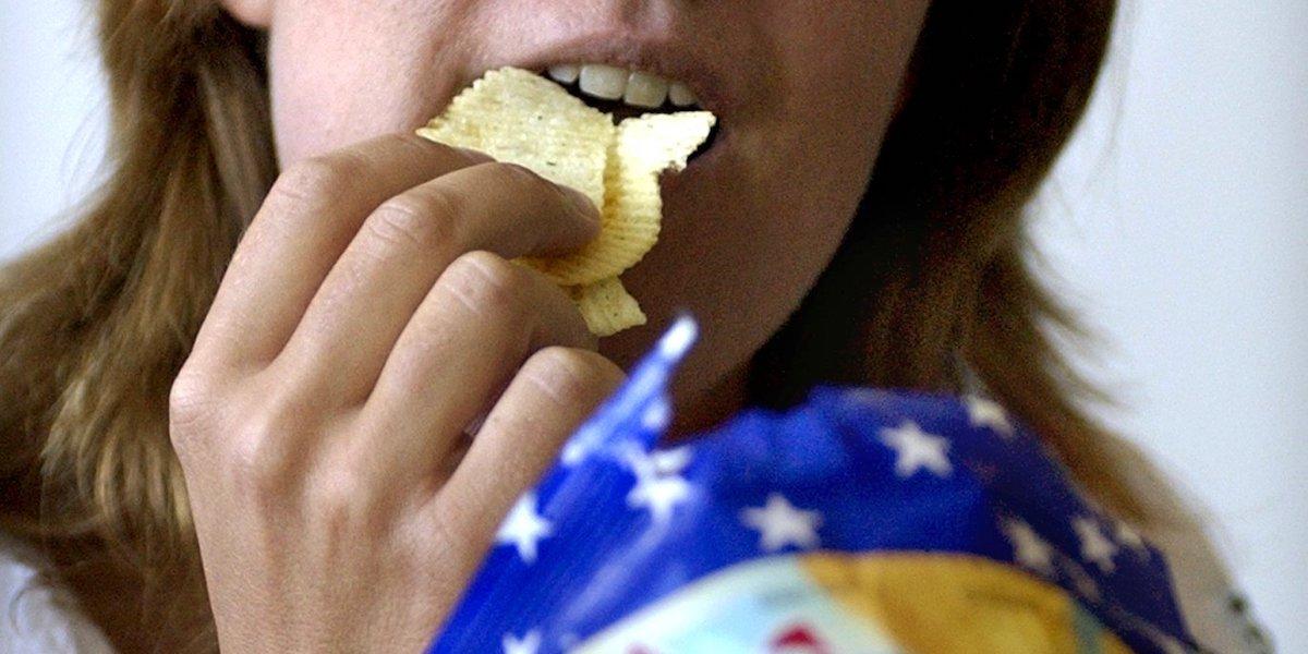 En kvinna äter chips. Chips och andra salta snacks är inte bra för ditt blodtryck