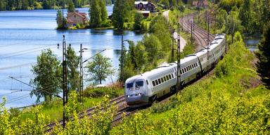 Ett tåg kör genom ett sommarlandskap. SJ släpper massor av extra sommarbiljetter i juli.