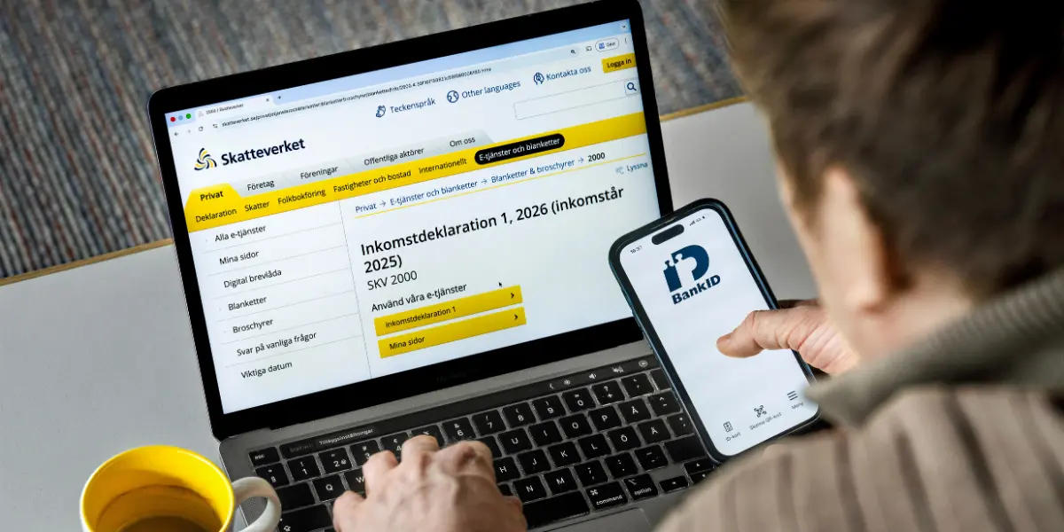 En man framför en dator med mobil i handen genomför en deklaration.