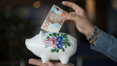 En hand som stoppar en sedel i en spargris.