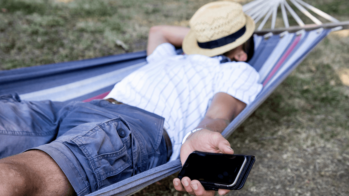 En man som sover i en hängmatta med en mobil i handen.